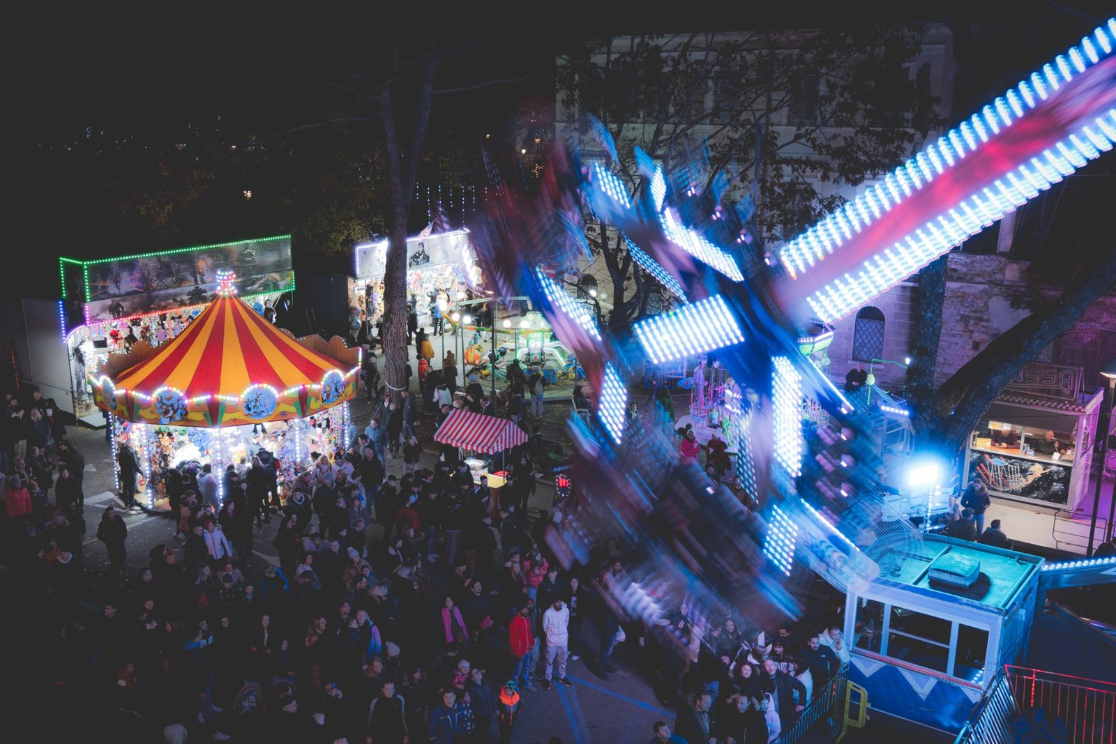 A night fair seen from above, with a spinning ride lit up in blue